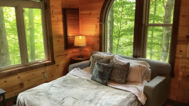A wooden cabin bedroom with a bed, pillows, a nightstand, and a lamp. - Tanzanite-- The "GEM" with a Hot Tub & WiFi!! (Slade)