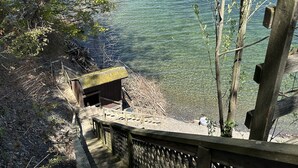 Eine Holztreppe führt zu einem Steg an einem klaren See, umgeben von Bäumen und einem Hollergel.