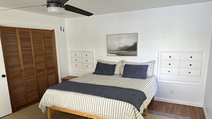 Ein Schlafzimmer mit Bett, Holzboden, Deckenventilator, Kleiderschrank und einem Bild an der Wand.