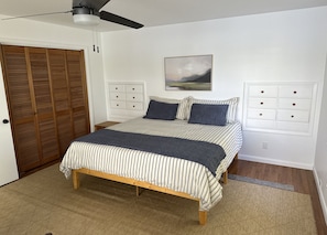 Une chambre à coucher avec un lit, un plancher en bois, un ventilateur de plafond, une armoire et un tableau au mur.