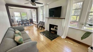 Ein Wohnzimmer mit grauem Sofa, Kamin, Fernseher und großen Fenstern.