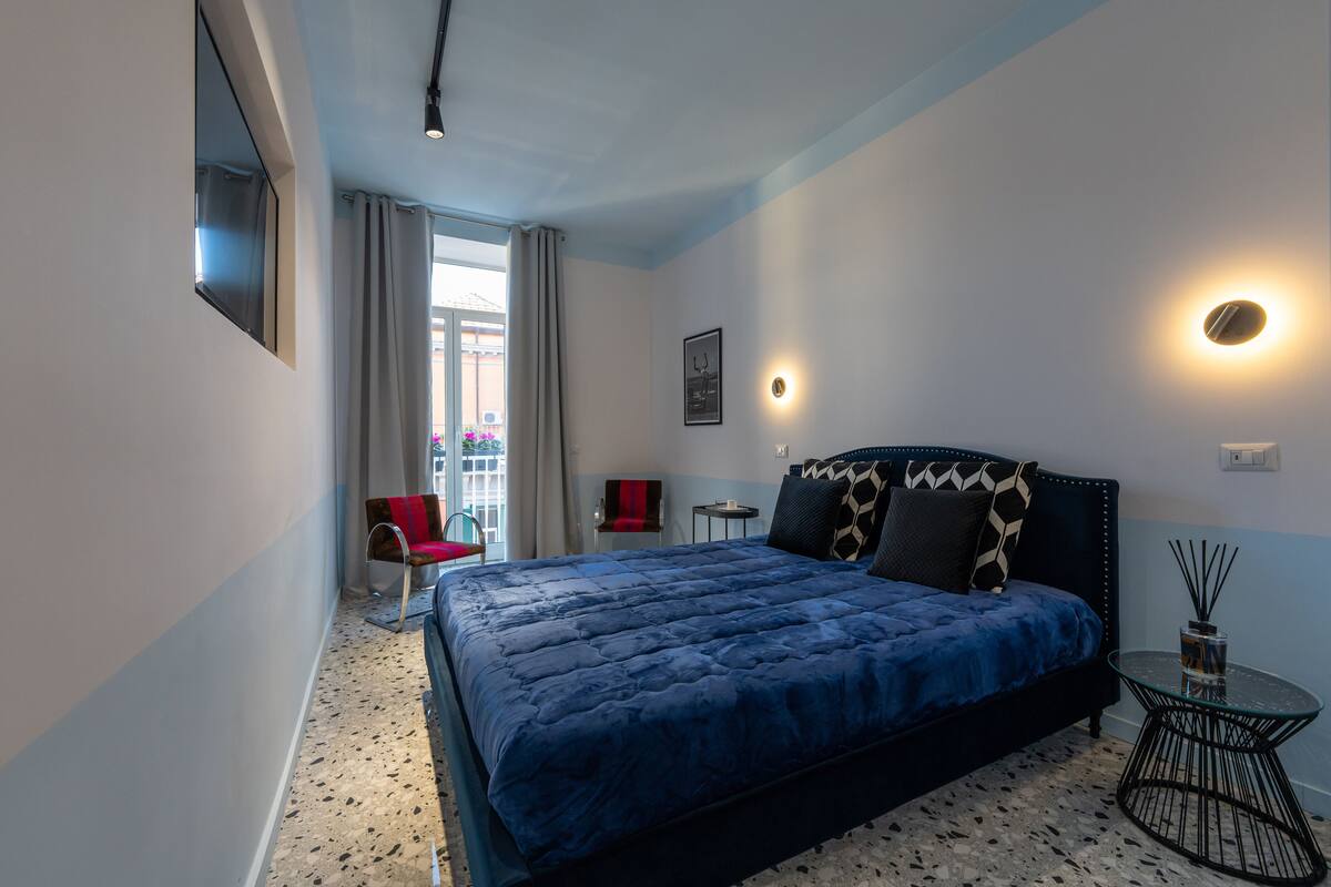 A modern hotel room with a large bed, a small table, a chair, and a TV mounted on the wall.