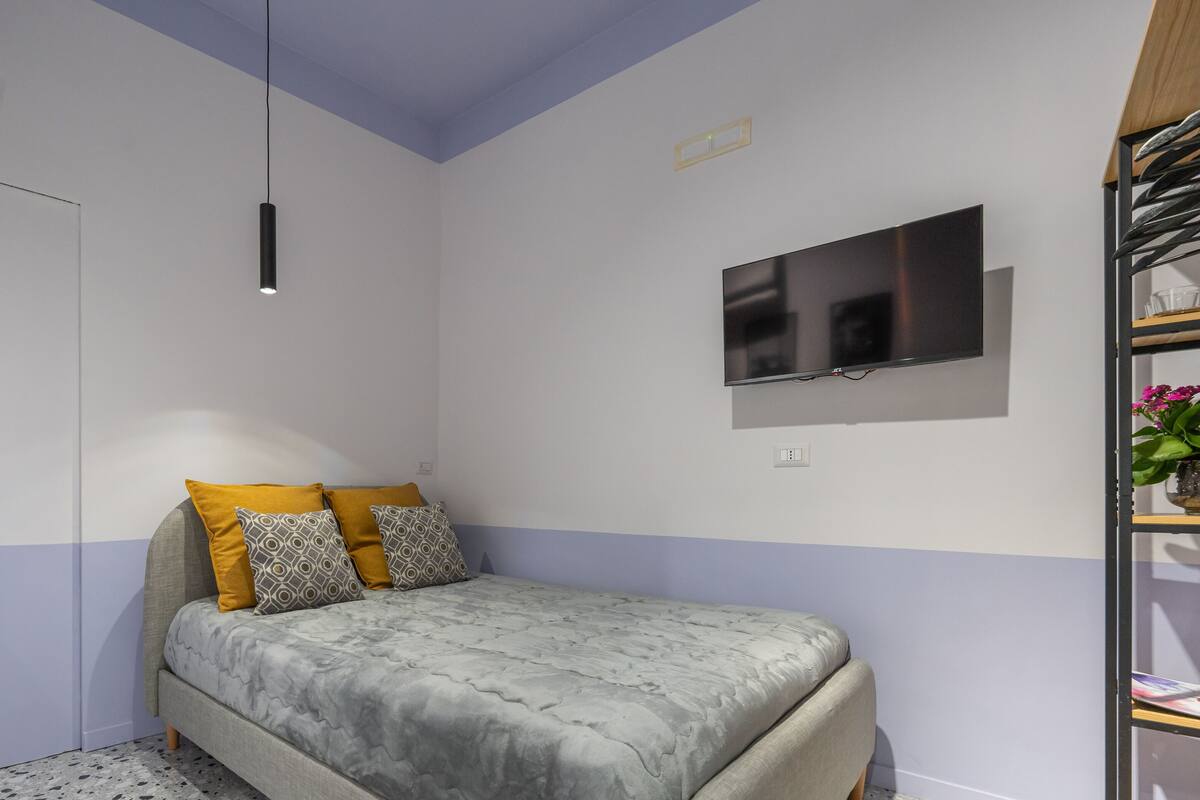 A bedroom with a bed, a TV mounted on the wall, and a bookshelf.