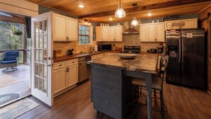 A spacious kitchen with wooden cabinets, a central island, stainless steel appliances, and a large window overlooking a deck.