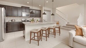 A modern kitchen with dark cabinets, a central island with bar stools, a built-in oven, and a microwave. - Stylish 5-BR Townhouse, PVT Pool,  Just Walk to the Clubhouse! (Davenport)