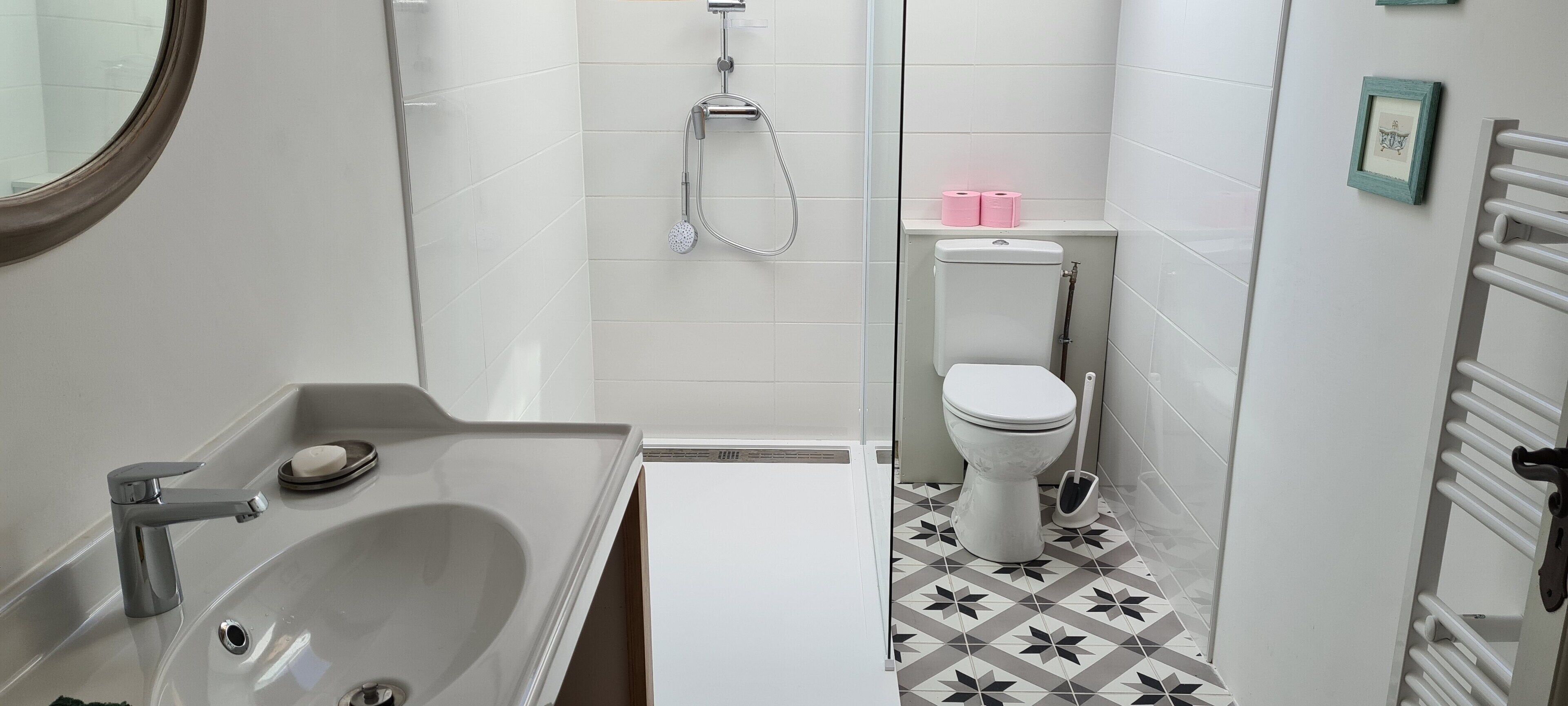 Et badeværelse med håndvask, toilet, bruser og et håndklædestativ.