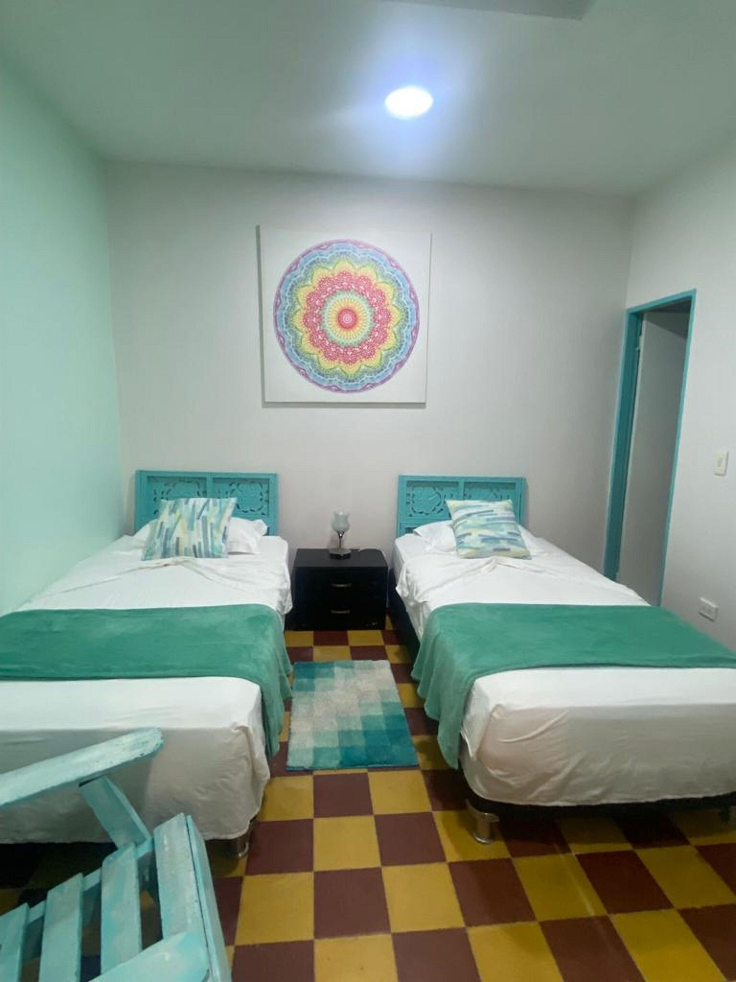 Een kamer met twee bedden, een geruit vloertapijt en een kleurrijk kunstwerk aan de muur.