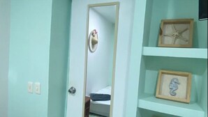 A room with a white door, a mirror, and a shelf with framed pictures.