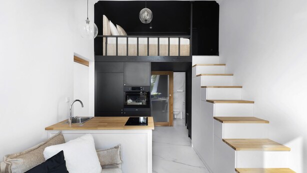 Ein kompaktes Studioapartment mit einer Küchenzeile, einem Sofa, einem Essbereich und einer Treppe.