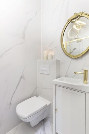 A bathroom with a toilet, a sink with a gold faucet, and a mirror with a gold frame. - Old Town Premium by Elite Apartments (Gdansk)