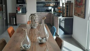 A modern kitchen with a wooden dining table, two glass vases with decorative items, and a large painting on the wall. - Mas Louis II (Vauvert)