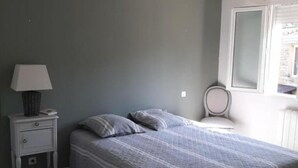 A bedroom with a bed, a nightstand, a lamp, a chair, and a window. - Mas Louis II (Vauvert)