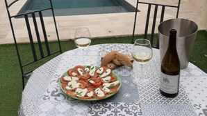 A poolside setting with a table set for two, featuring a plate of appetizers and a bottle of wine. - Mas Louis II (Vauvert)
