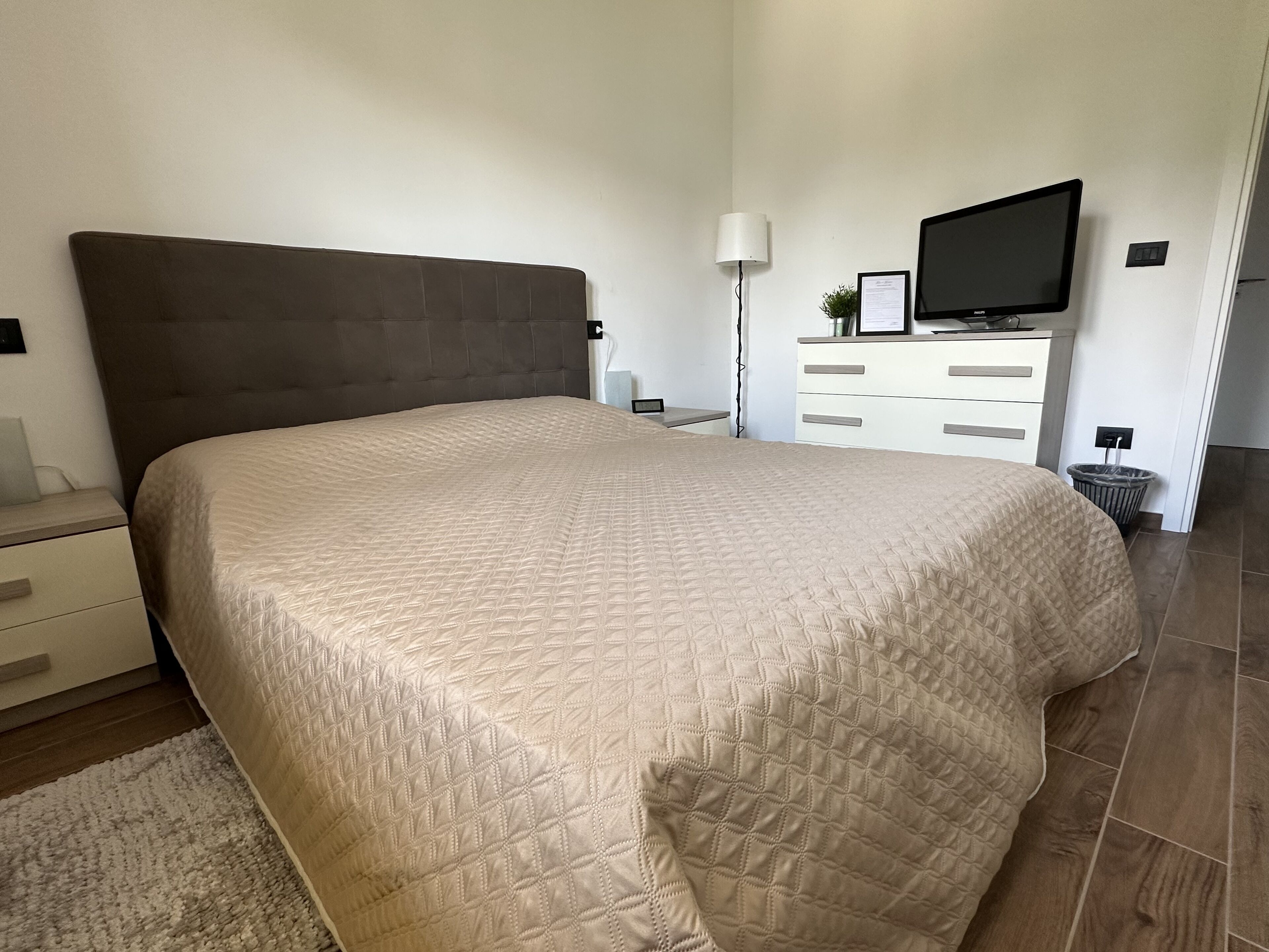 A bedroom with a large bed, a bedside table, a lamp, a TV, and a dresser.