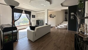 Een moderne woonkamer met een witte bank, een flatscreentelevisie en een groot raam met gordijnen.