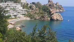 Une ville côtière avec des bâtiments construits sur une colline, un promontoire rocheux surmonté d’une tour et une mer d’un bleu limpide.