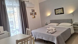 Une chambre d’hôtel avec un lit, un bureau et une chaise. Il y a des tableaux au mur et une fenêtre avec des rideaux.