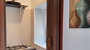 Une cuisine équipée d’une cuisinière à gaz, d’un luminaire suspendu et d’une étagère fixée au mur.