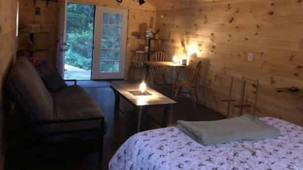 En mysig stuga med en säng, ett bord med ett tänt ljus, en soffa och en matplats med stolar.