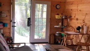 En mysig stuga med träinredning, ett matbord med stolar, en soffa och ett stort fönster med utsikt över skogen.