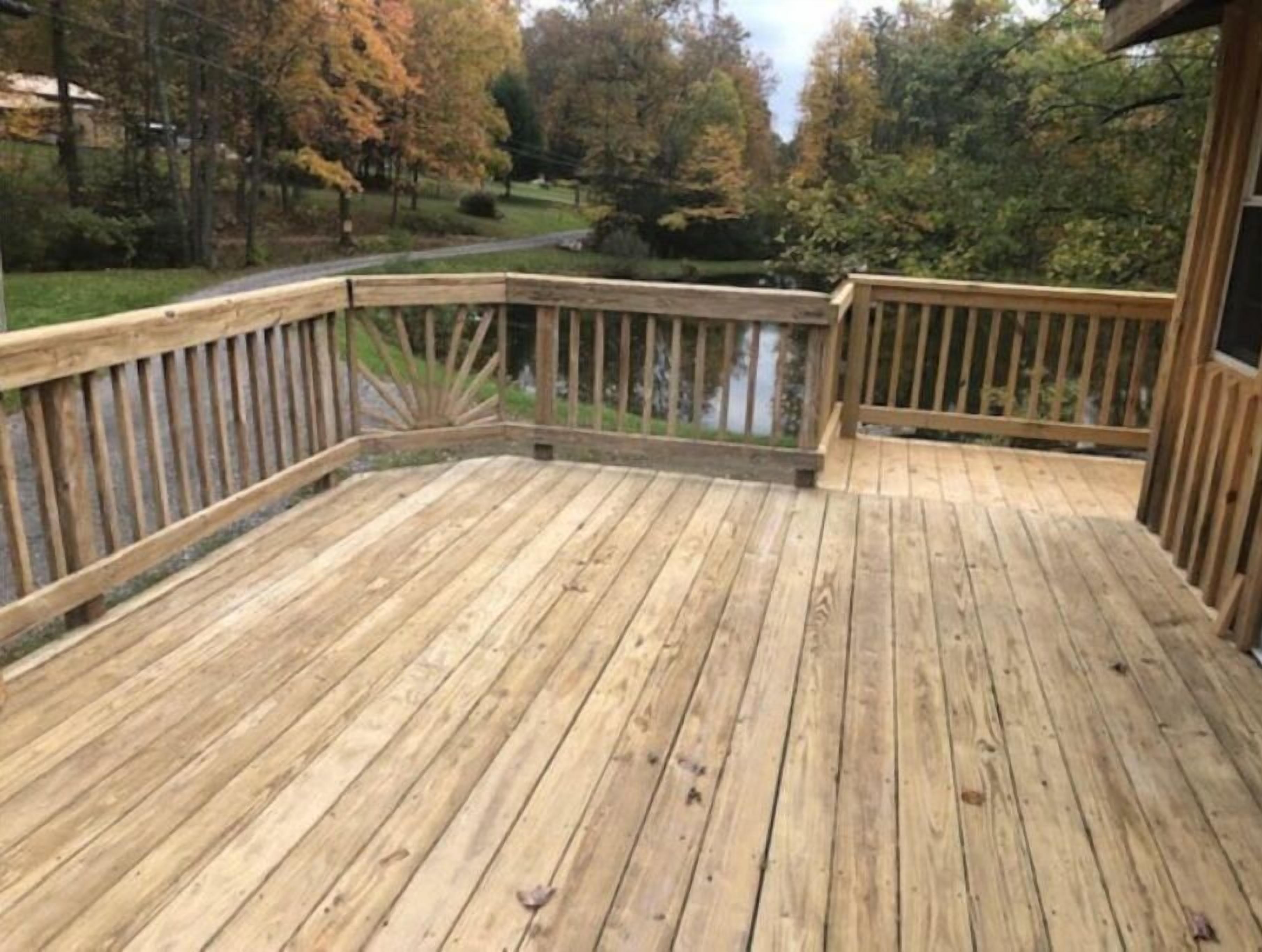 A wooden deck with a railing, overlooking a river and trees.