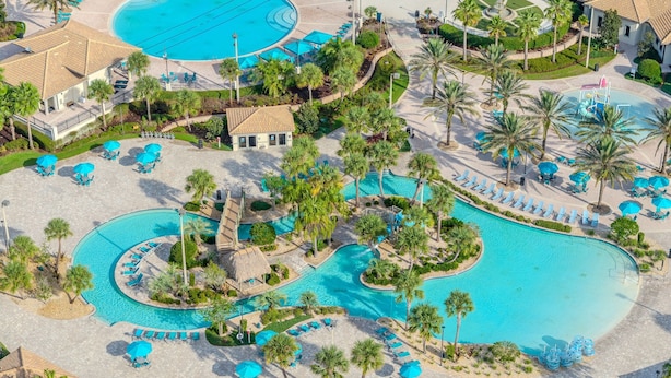 Ett flygbildsfoto av ett semesterområde med flera pooler, palmer och solstolar.