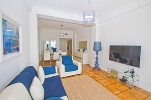 Ein modernes Wohnzimmer mit einer Couch, Sesseln, einem Fernseher und einem Glastisch.