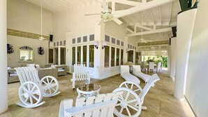 A spacious indoor area with white rocking chairs and tables, large windows, and a high ceiling with exposed beams. - "srvittinivillas Great / Family / Trip Team/ Caribbean Dr" (San Rafael del Yuma)