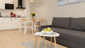 Une cuisine moderne avec des meubles blancs, un coin repas avec une table et des chaises blanches, et un canapé gris dans l’espace salon.