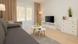 Un salon moderne avec un canapé gris, un téléviseur posé sur un meuble, une petite table sur laquelle se trouvent des fruits et un buffet blanc.