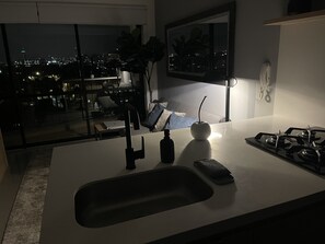 Eine moderne Küche mit einer großen Kochinsel, einer Spüle und einem Herd. Durch große Fenster bietet sich ein Blick auf die Stadt.
