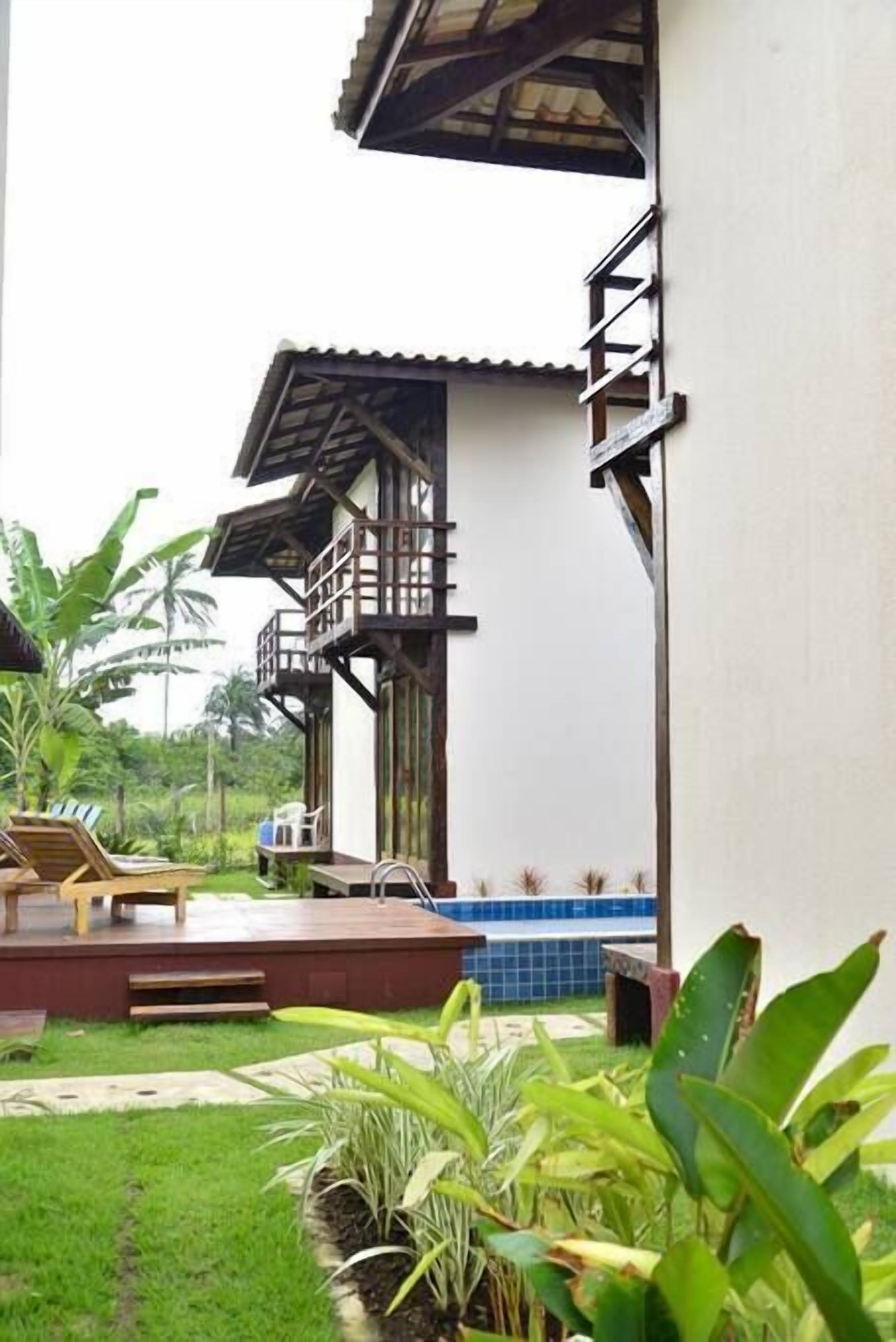 A building with a balcony, a pool, and a garden with tropical plants.