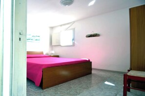 A bedroom with a wooden bed, a nightstand, a window, and a door. - Alba Two-room Air-conditioned Holiday Home for 4 Guests (Melendugno)
