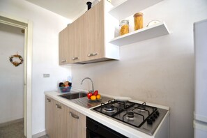 A kitchen with a gas stove, a sink, wooden cabinets, and a bowl of fruit on the counter.
