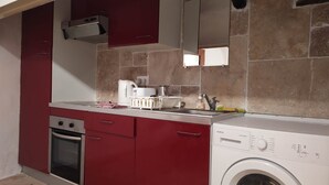 A compact kitchen with a built-in oven, a washing machine, and a red cabinet. - Attractive, Renovated Village House in Traffic-free Street (Estagel)
