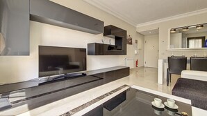 Een moderne woonkamer met een flatscreen televisie, een geïntegreerde keuken en een eethoek met stoelen en een tafel.