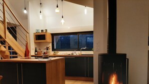 A modern kitchen with a central island, wooden staircase, and a wood-burning stove. - Seaside house (La Turballe)