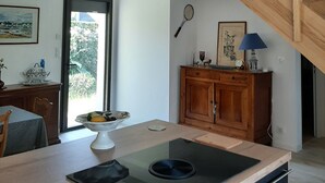 A modern kitchen with a central island, wooden staircase, and a view of greenery outside. - Seaside house (La Turballe)