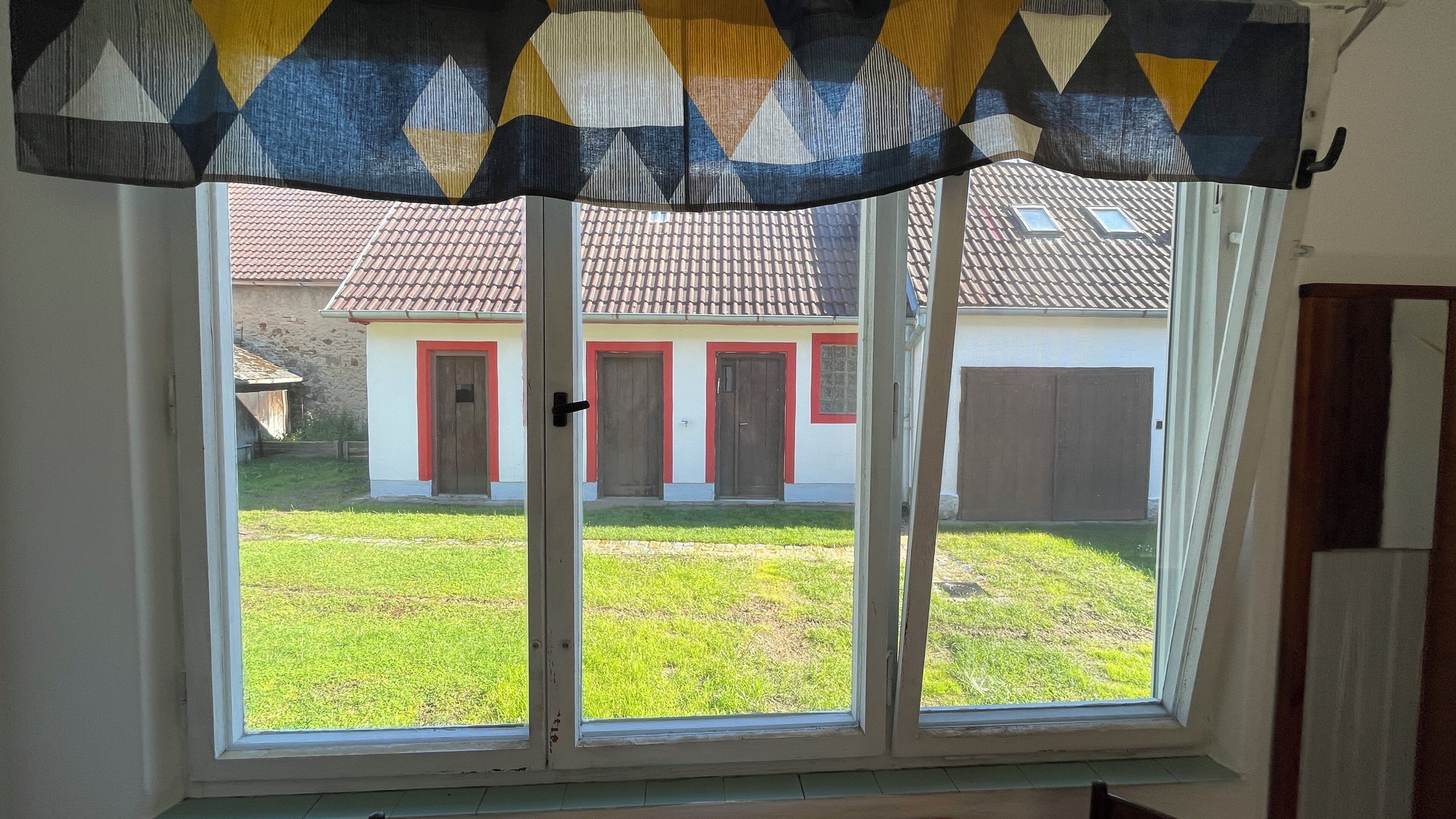 Une pièce dotée d’une grande fenêtre donnant sur une maison avec une porte rouge et un garage.