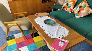 Een kamer met een houten tafel, een kleurrijk tapijt, een groene bank en een boek getiteld 'Dikobraz'.