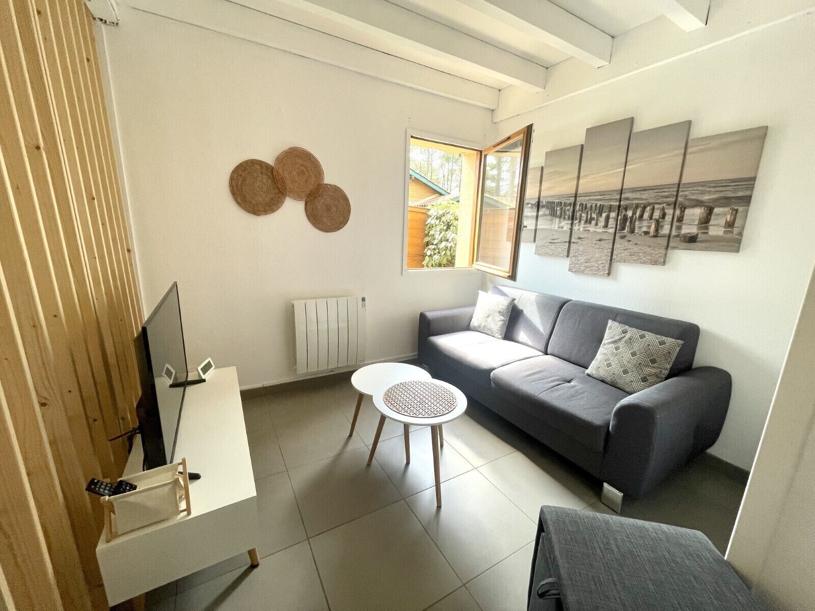 Un salon moderne avec un canapé gris, une petite table ronde et un téléviseur posé sur un meuble.