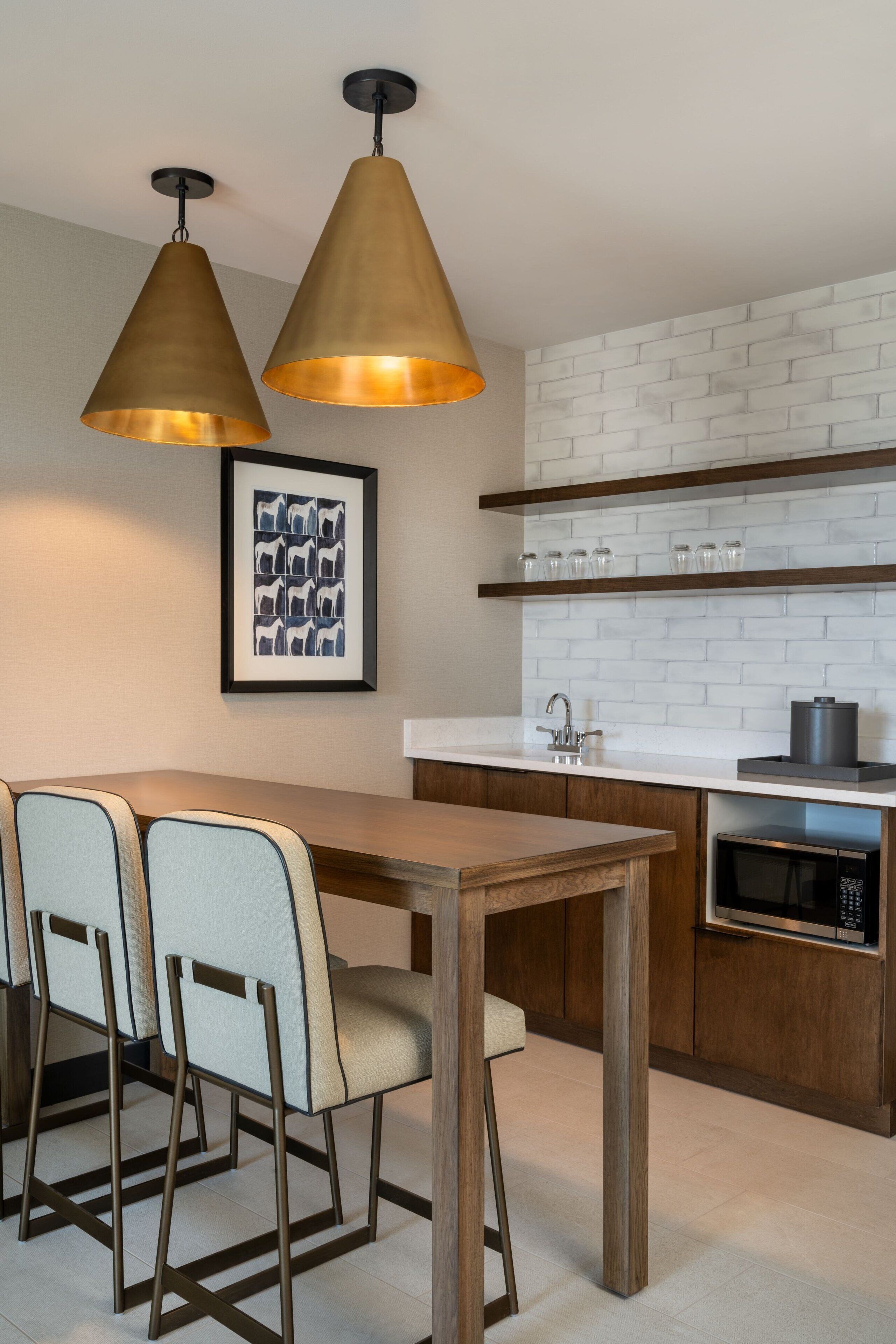 Une cuisine moderne avec un mur de fond en briques blanches, des armoires en bois, un four à micro-ondes en acier inoxydable et des luminaires suspendus.