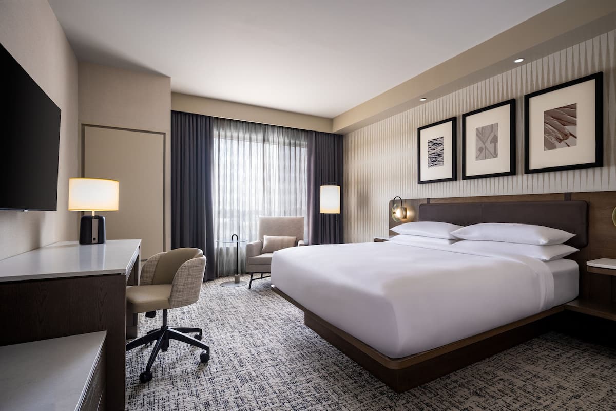 A hotel room with a large bed, a desk, a chair, and a TV.
