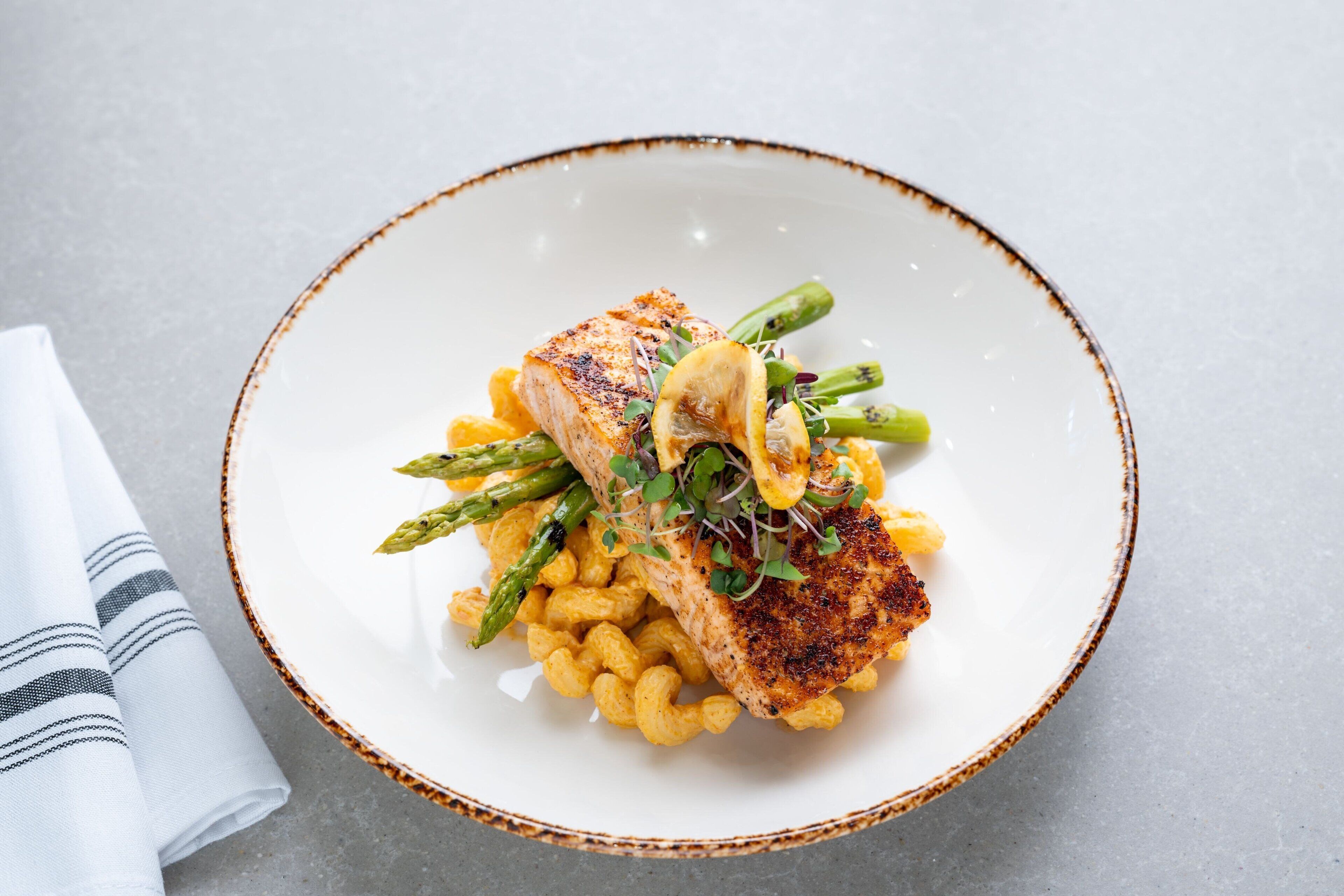 A plate of food with a piece of grilled fish, asparagus, and macaroni.