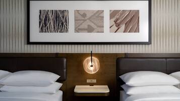 Een hotelkamer met twee bedden, een nachtkastje, een lijst met kunstwerk erboven en een wandlamp.