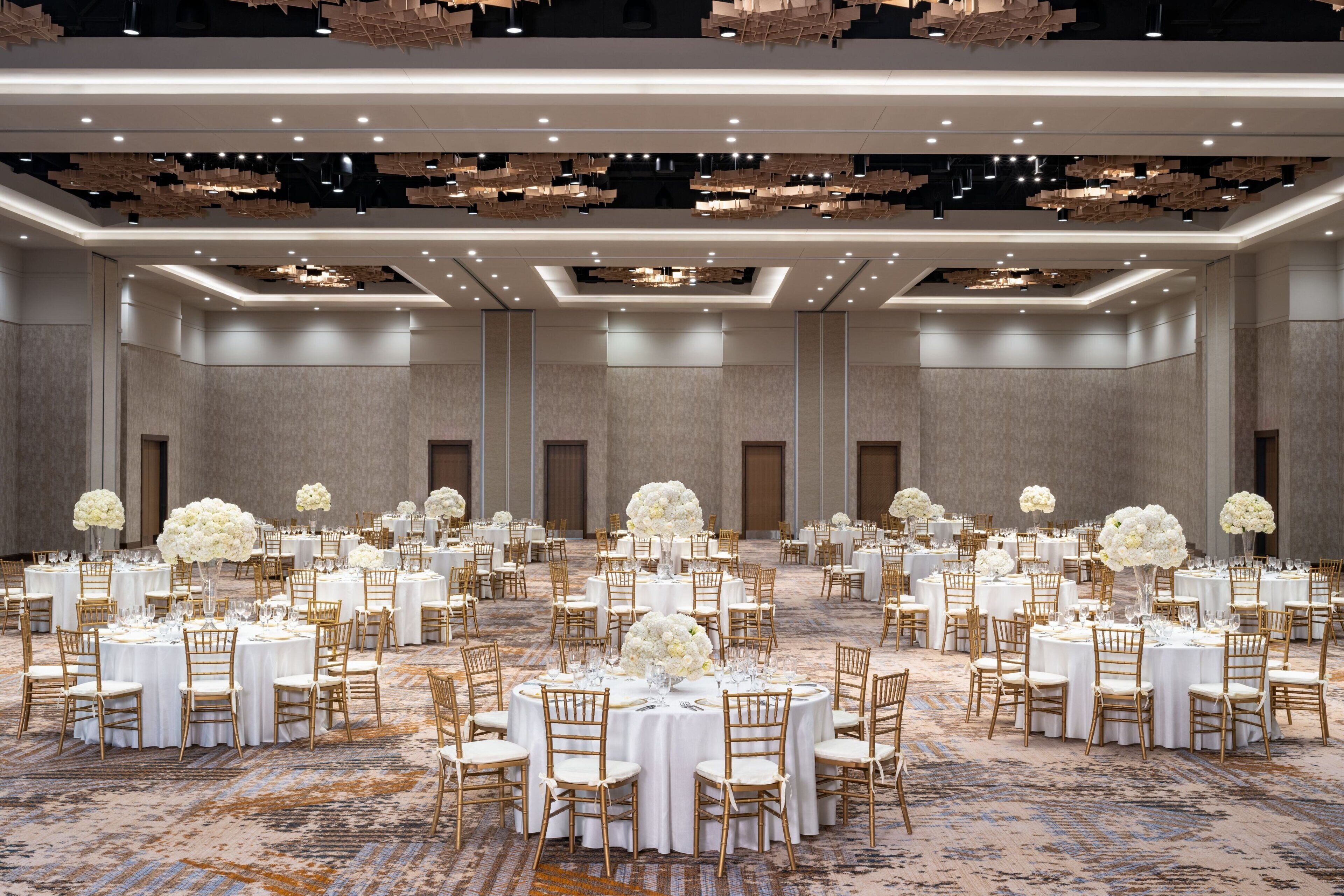 A large banquet hall with round tables, white tablecloths, and gold chairs.