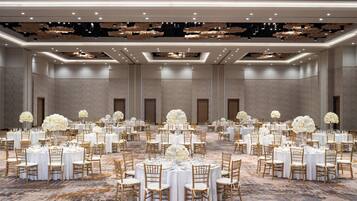A large banquet hall with round tables, white tablecloths, and gold chairs.