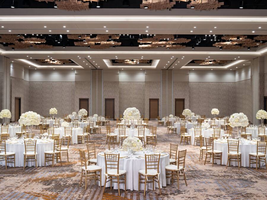 A large banquet hall with round tables, white tablecloths, and gold chairs.