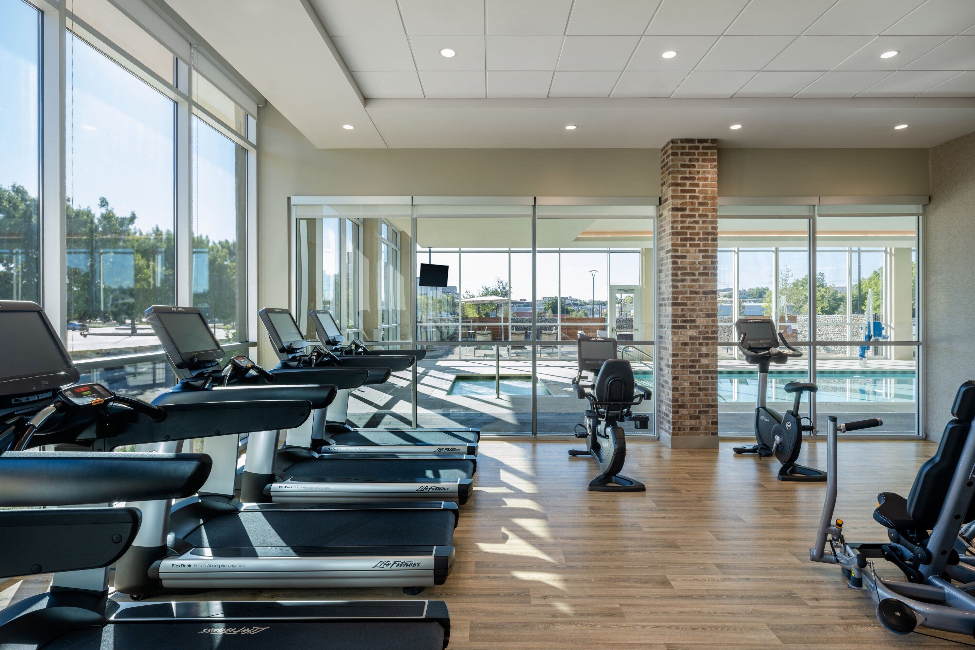 A modern gym with treadmills, stationary bikes, and a brick pillar.