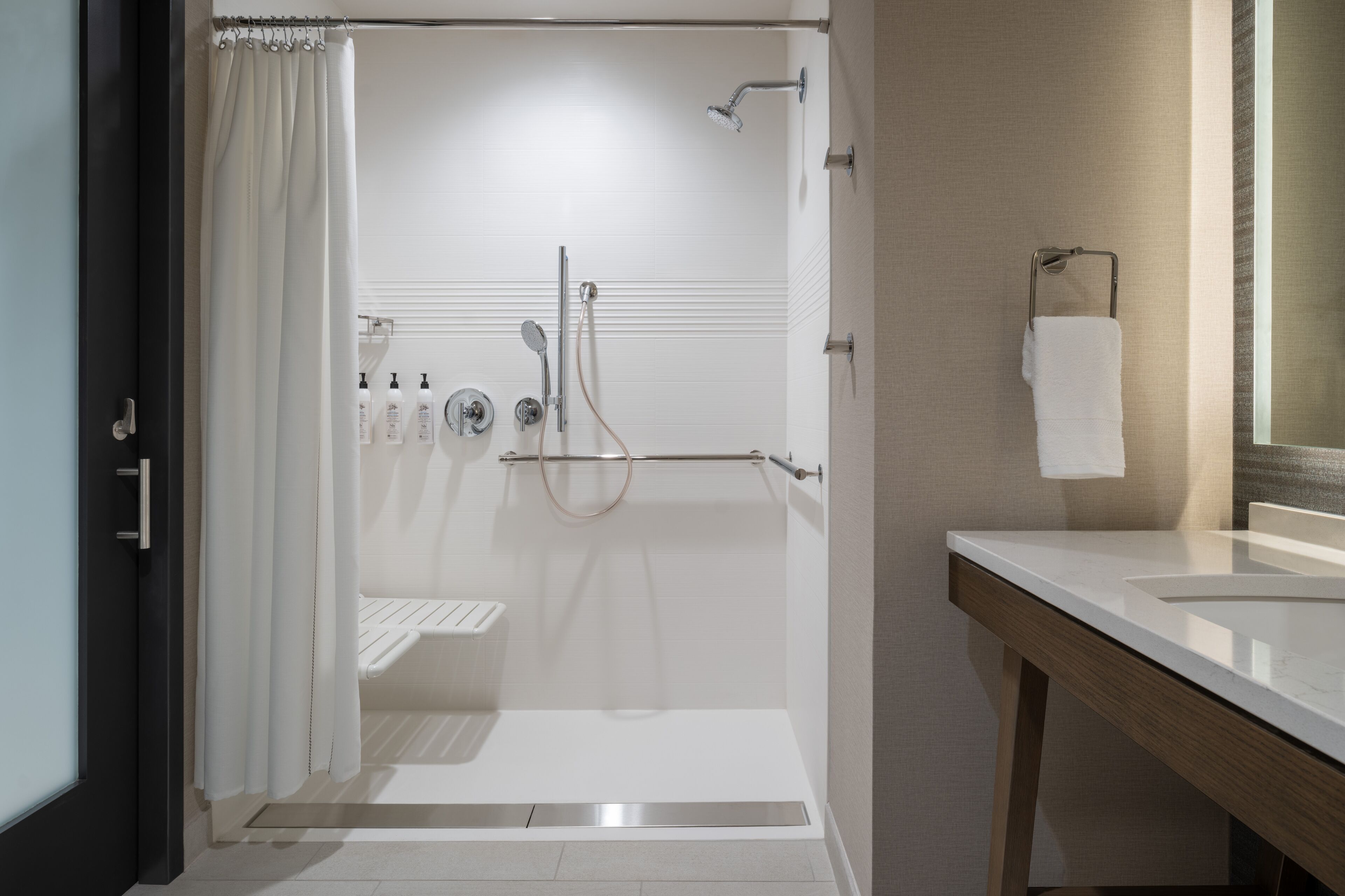 Een moderne badkamer met een glazen douchecabine, een witte wastafel en een handdoekhouder.